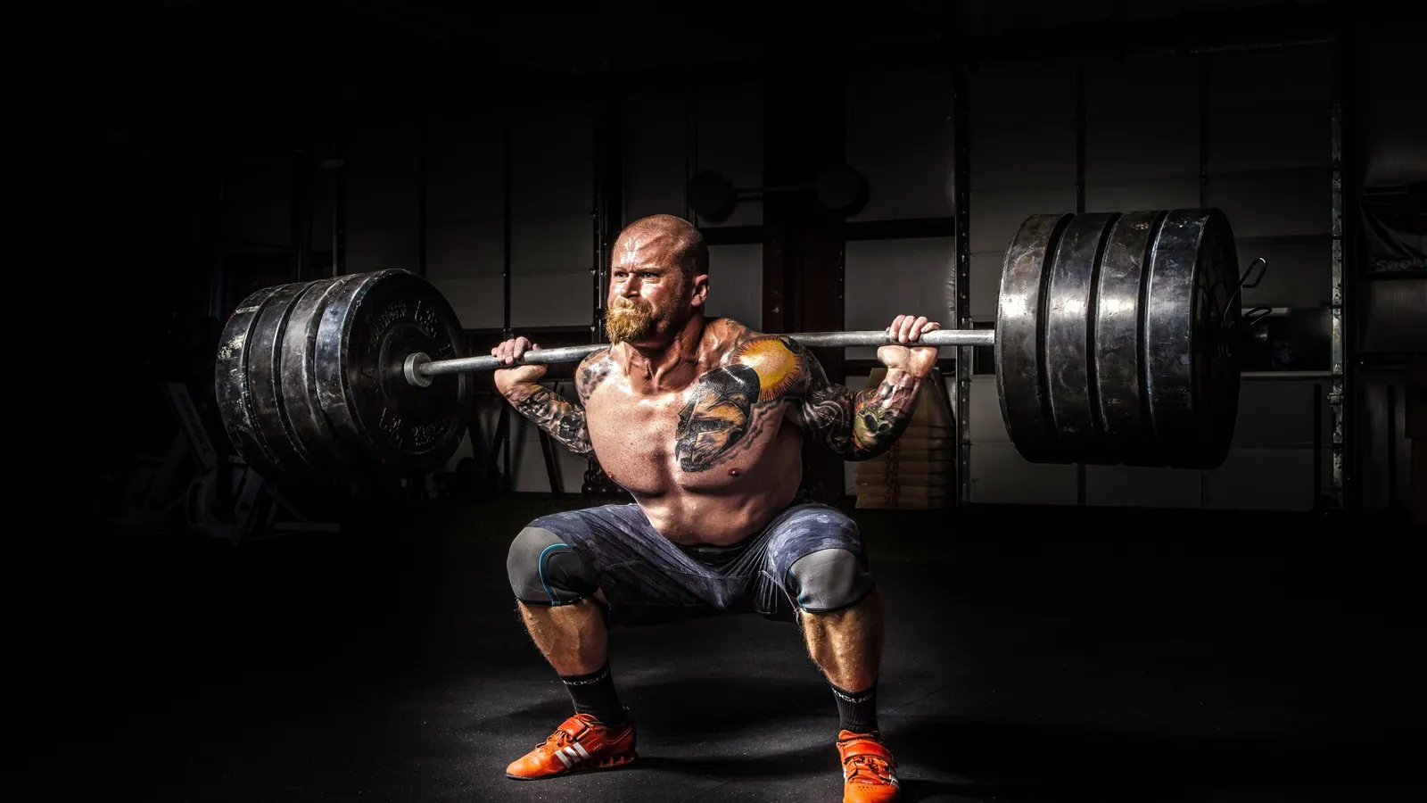 Athlète en position basse de squat avec une barre chargée sur les épaules dans une salle sombre