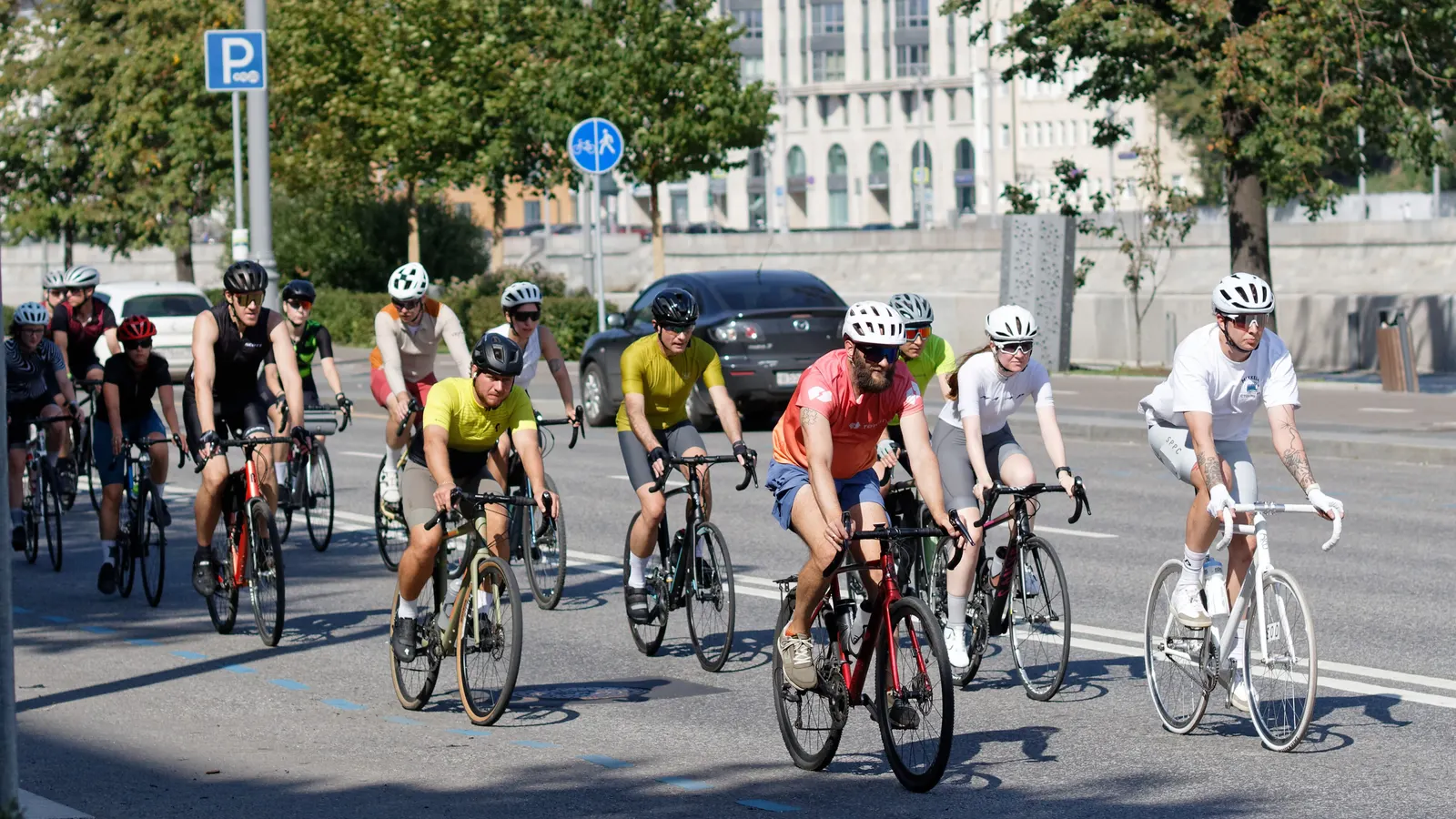 Groupe de cyclistes sur route roulant en peloton serré dans une rue bordée d'arbres