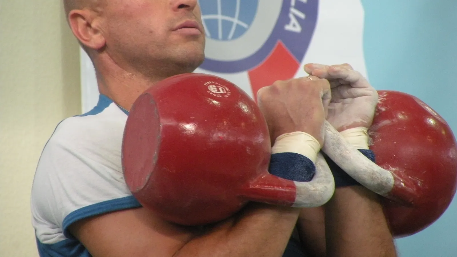 Athlète portant deux kettlebells rouges à hauteur d'épaules pendant un effort intense