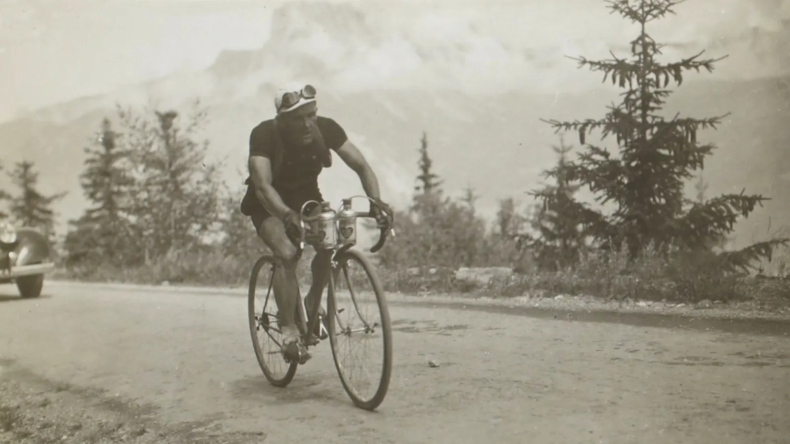 Coureur cycliste des années 1930 grimpant une route de montagne avec deux bidons accrochés au guidon